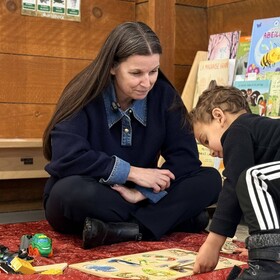 la directrice assise avec un élève qui fait un jeu au sol